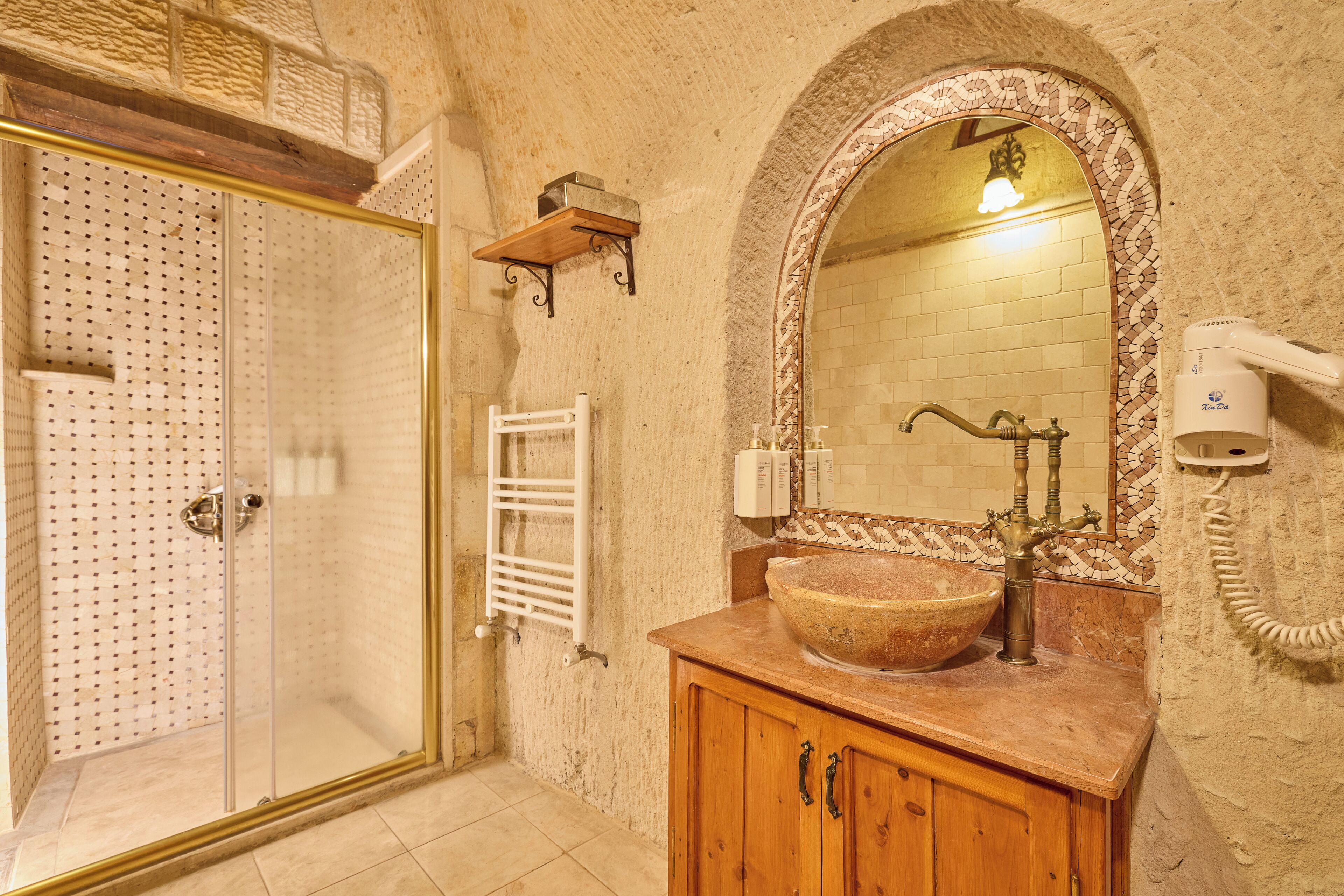 A bathroom with a glass shower enclosure, a wooden vanity with a large bowl sink, a mirror with an ornate frame, and a towel rack.