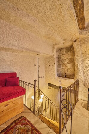 A room with a stone wall, a wooden bed with red bedding, and a staircase with a metal railing.