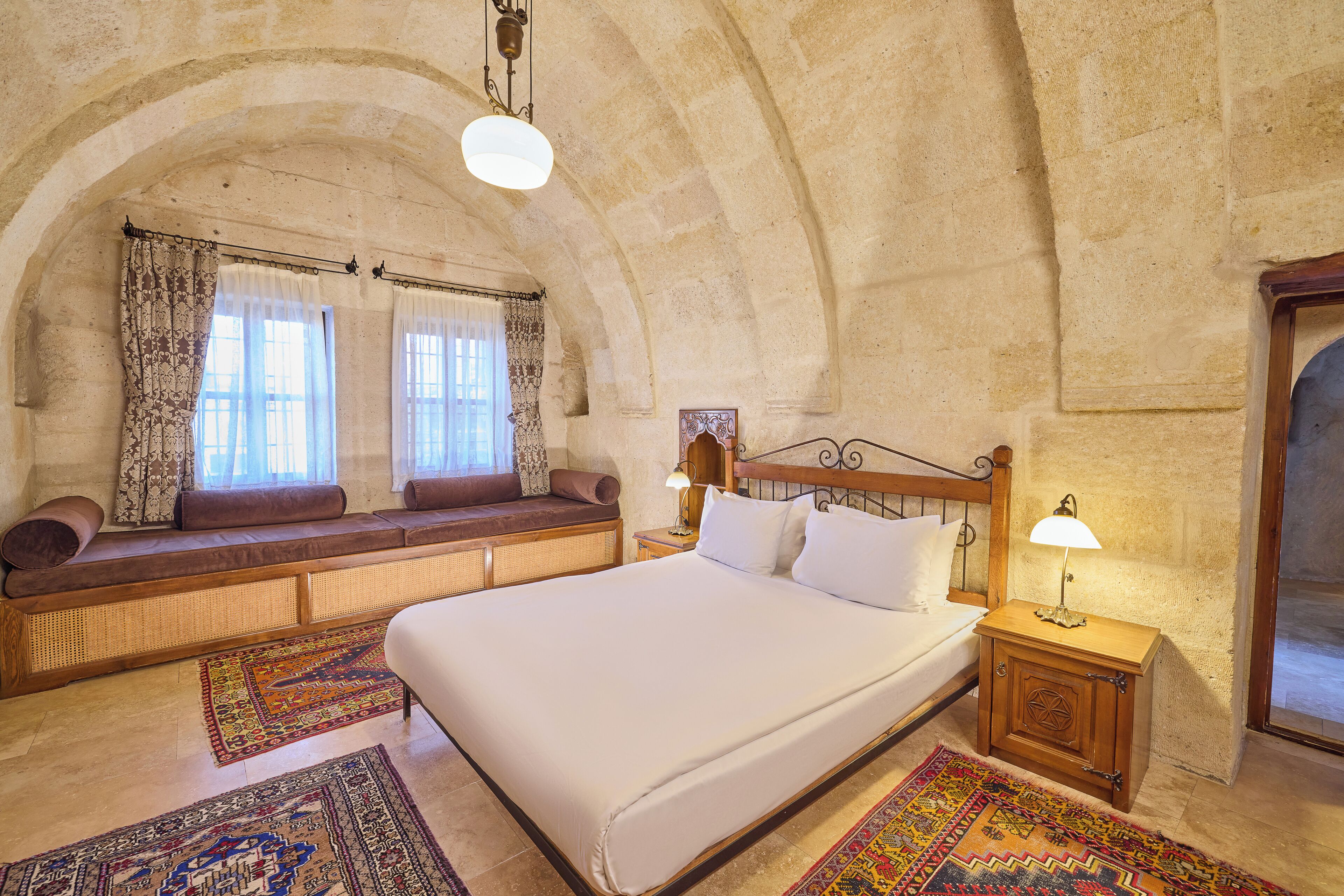 A spacious room with a large bed, a bench with cushions, and a small table with a lamp.