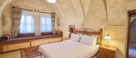 A spacious room with a large bed, a bench with cushions, and a small table with a lamp.