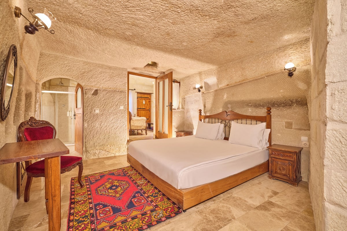 A bedroom with a wooden bed, a red chair, a small table, and a patterned rug.