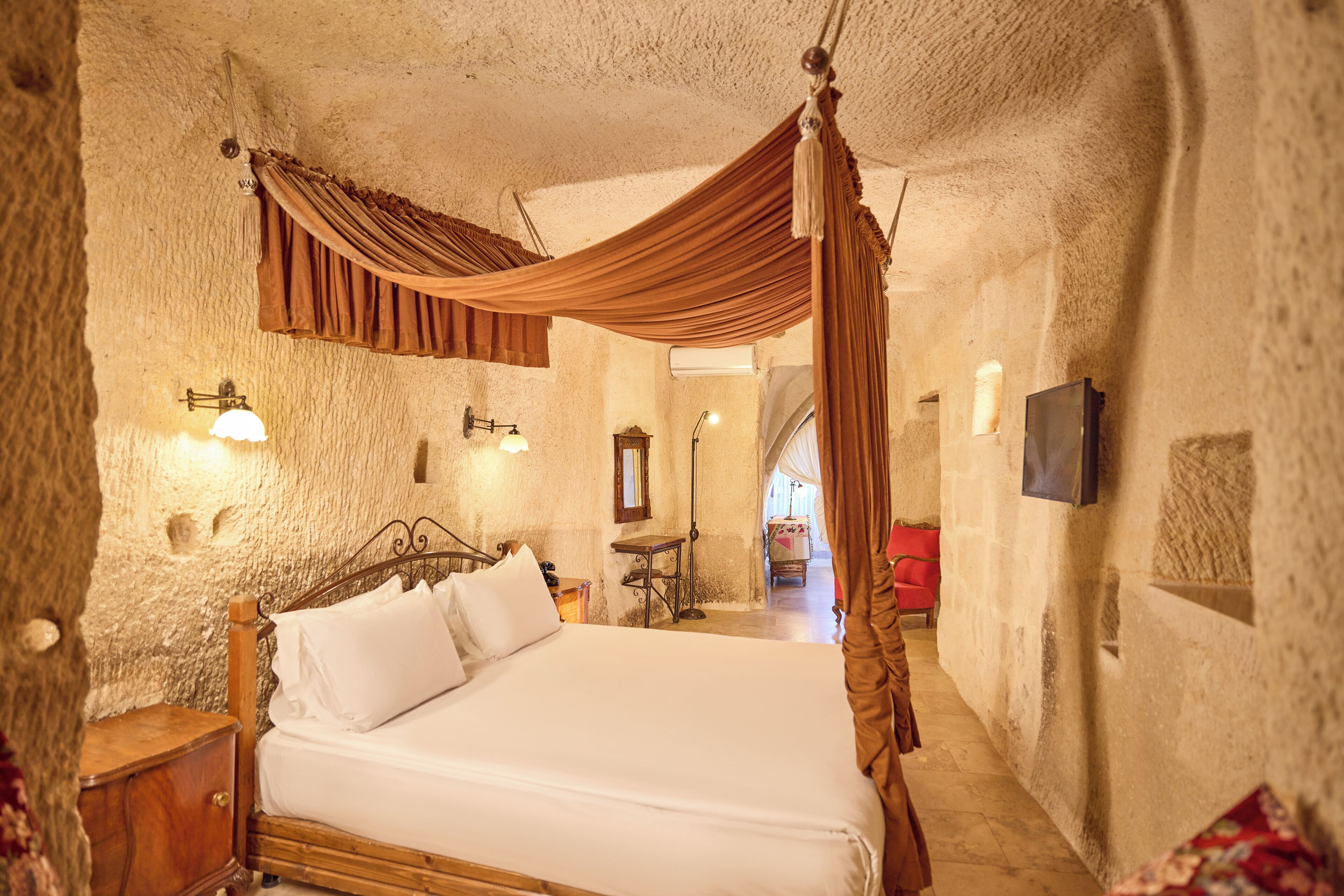 A bedroom with a four-poster bed, a nightstand, a wooden chair, a small table, and a mirror on the wall.