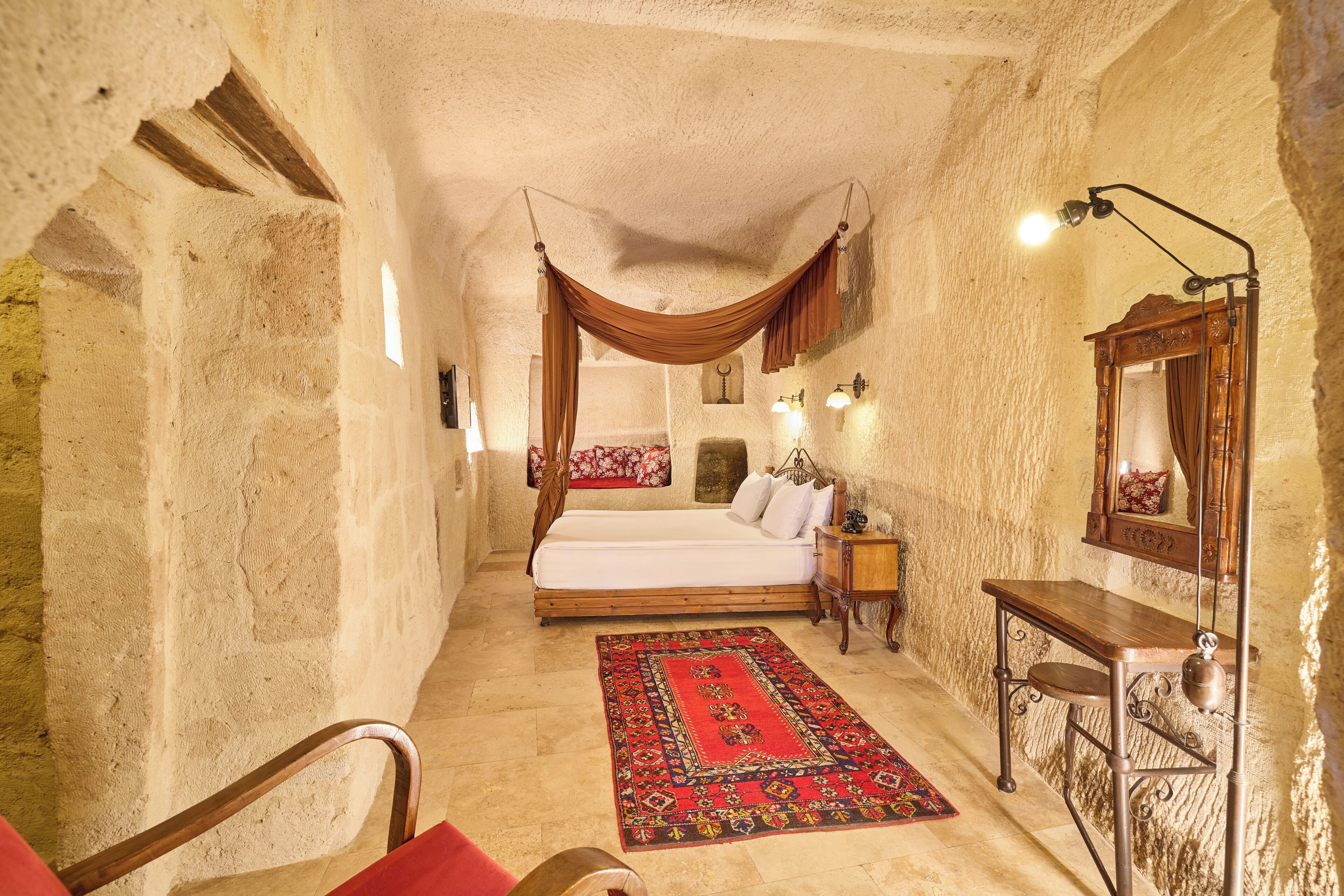 Ein Schlafzimmer mit einem Bett, einem Nachttisch aus Holz, einem Spiegel und einem roten Teppich mit Muster.