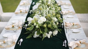 Een gedekte tafel voor een formeel evenement buiten, met wit servies en een groene tafelkleed.