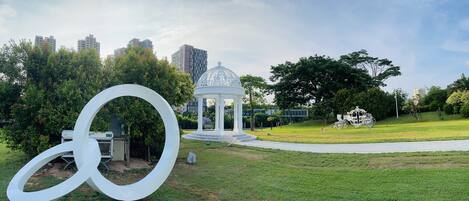 A park with a gazebo, a large white sculpture, and a cityscape in the background.