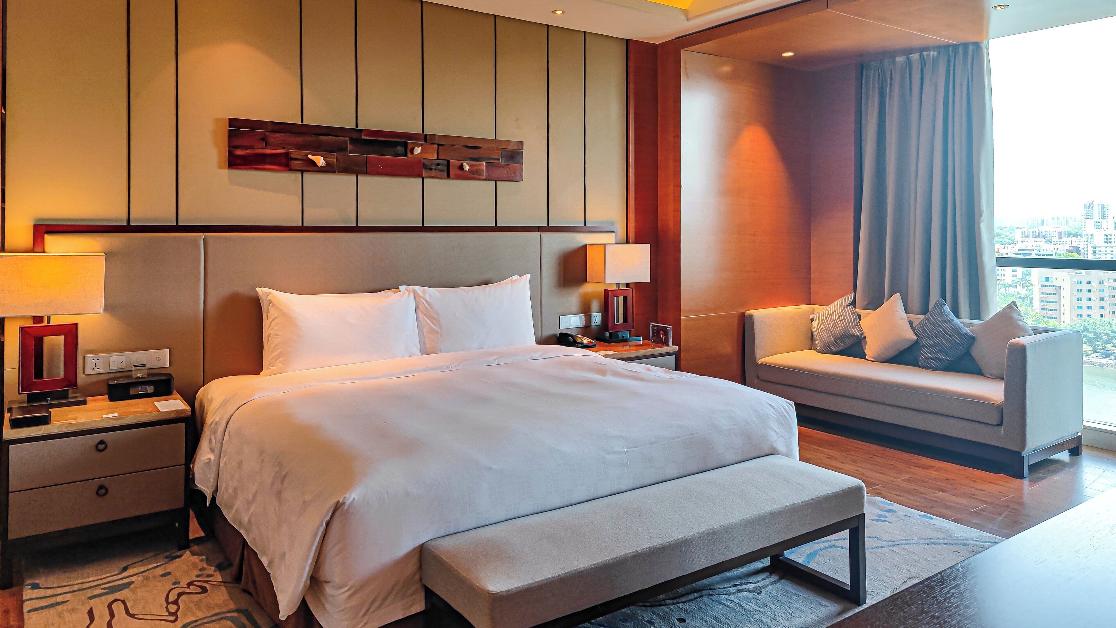 A hotel room with a large bed, bedside tables, a sofa, and a view of the city.