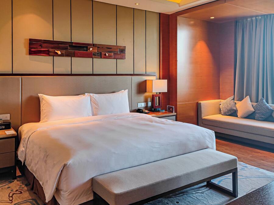 A hotel room with a large bed, bedside tables, a sofa, and a view of the city.