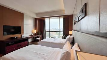 A hotel room with two beds, a desk, a television, and a large window.