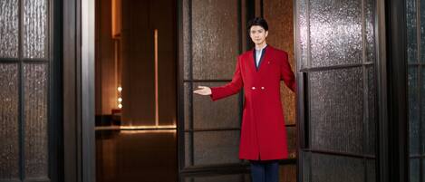 A man in a red coat standing in a hallway with wooden paneling and a polished floor.