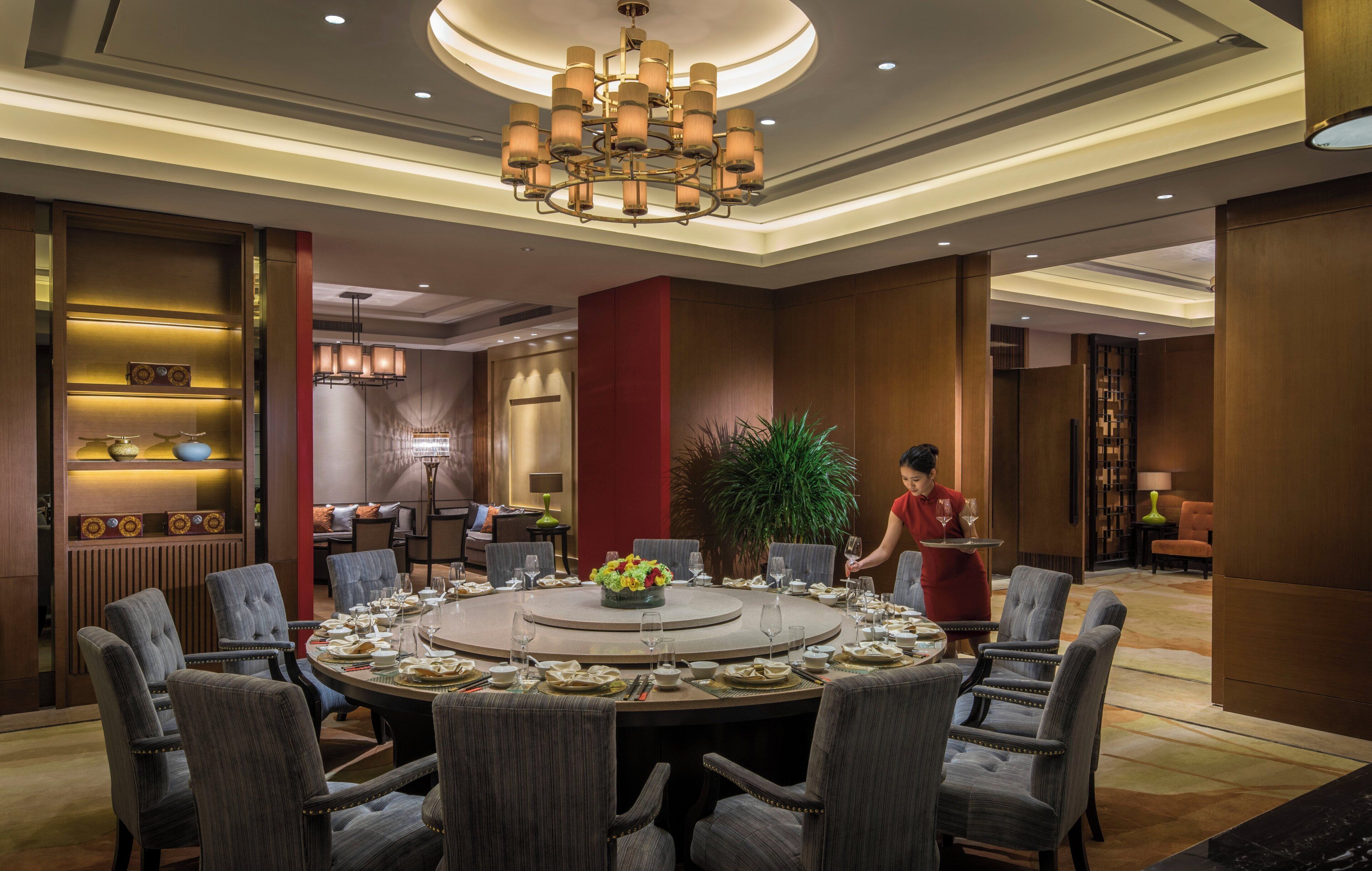 A formal dining area with a round table, multiple chairs, and a chandelier.