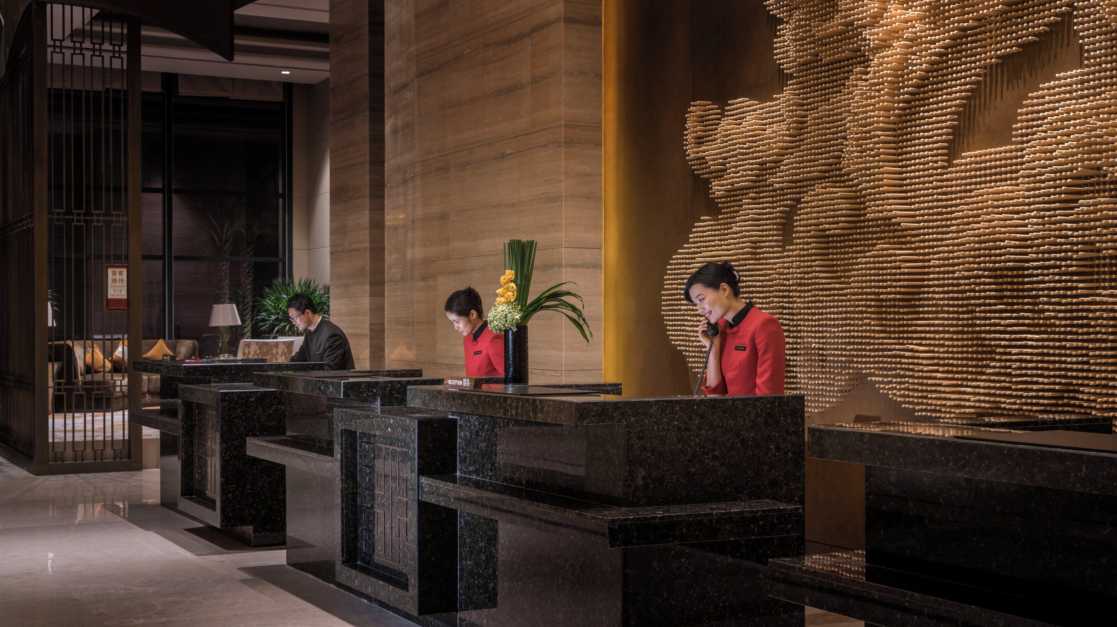 Una zona de recepción de hotel con mostradores de mármol, un mostrador de recepción y una pared decorativa.