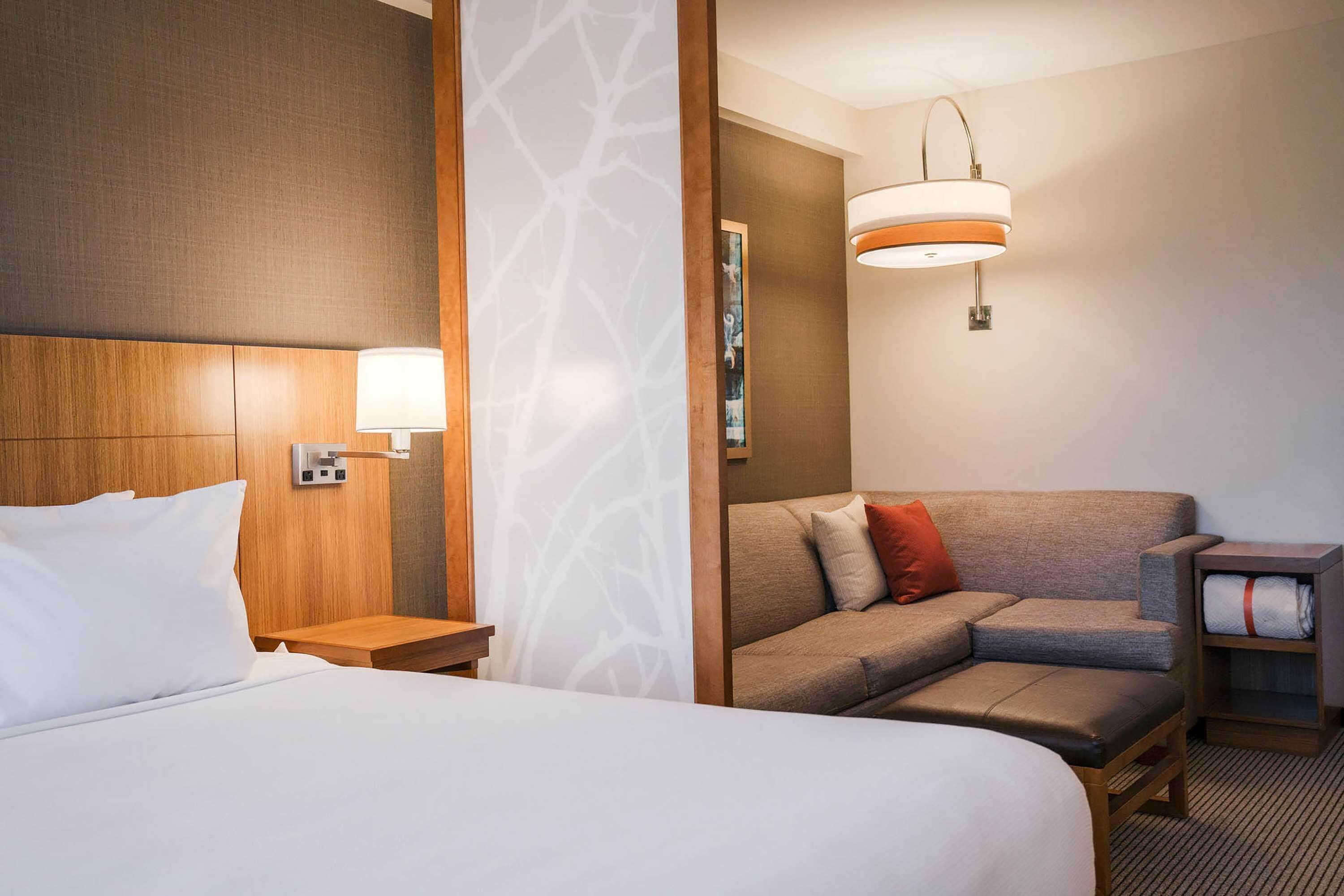 A hotel room with a large bed, a sofa, a nightstand, and a lamp.