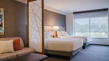 Habitación de hotel con una cama grande, un sofá, una mesita y vistas a árboles por la ventana.