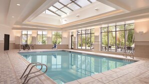 Une piscine intérieure dotée d’un plafond en verre transparent, de carrelages et de nombreuses fenêtres offrant une vue sur l’extérieur.