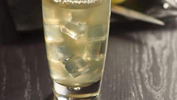 A glass of a clear beverage with ice cubes and a lime slice garnish, placed on a dark wooden surface.