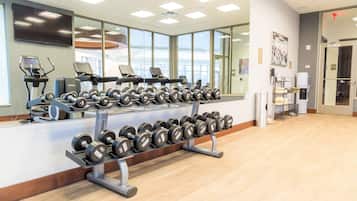A gym with cardio machines, dumbbells, and a large mirror.