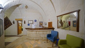 Vestíbulo con mostrador de recepción de piedra, una silla azul y una verde, y un espejo grande que refleja el interior.