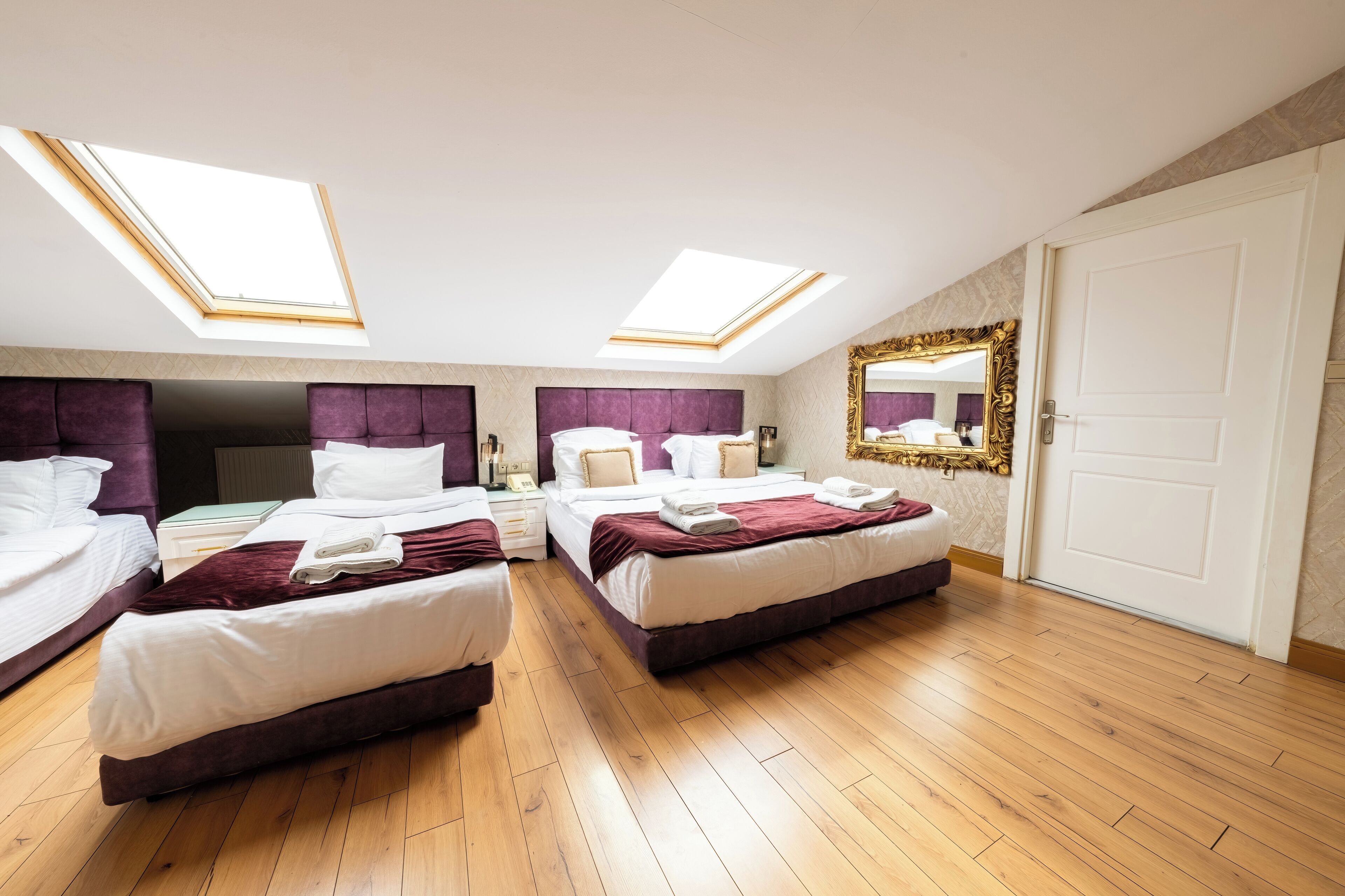 Ein Hotelzimmer mit zwei Betten, einem Oberlicht, einem großen Spiegel und einem Holzboden.