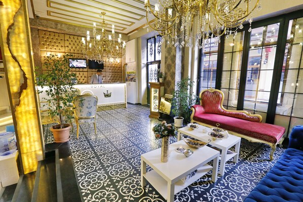 A luxurious lobby with a reception desk, a red sofa, a blue sofa, and a chandelier.
