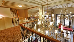 A grand staircase with a patterned carpet, a chandelier, and a red sofa in a well-lit room with a high ceiling and ornate details. - Diamond Royal Hotel (Istanbul)