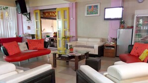 A living room with a red sofa, white sofa, and a glass coffee table. There is a television on the wall and a refrigerator in the corner. - Kea Valley Hotel Apartment (Brinchang)
