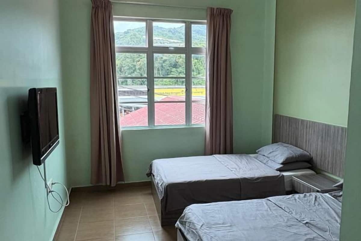 Una habitación con dos camas, un televisor montado en la pared y un ventanal con cortinas.