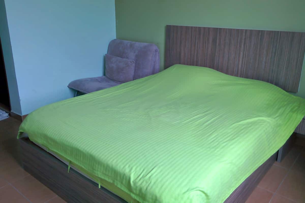 Una cama con una colcha verde en una habitación con cabecera de madera y una silla morada.