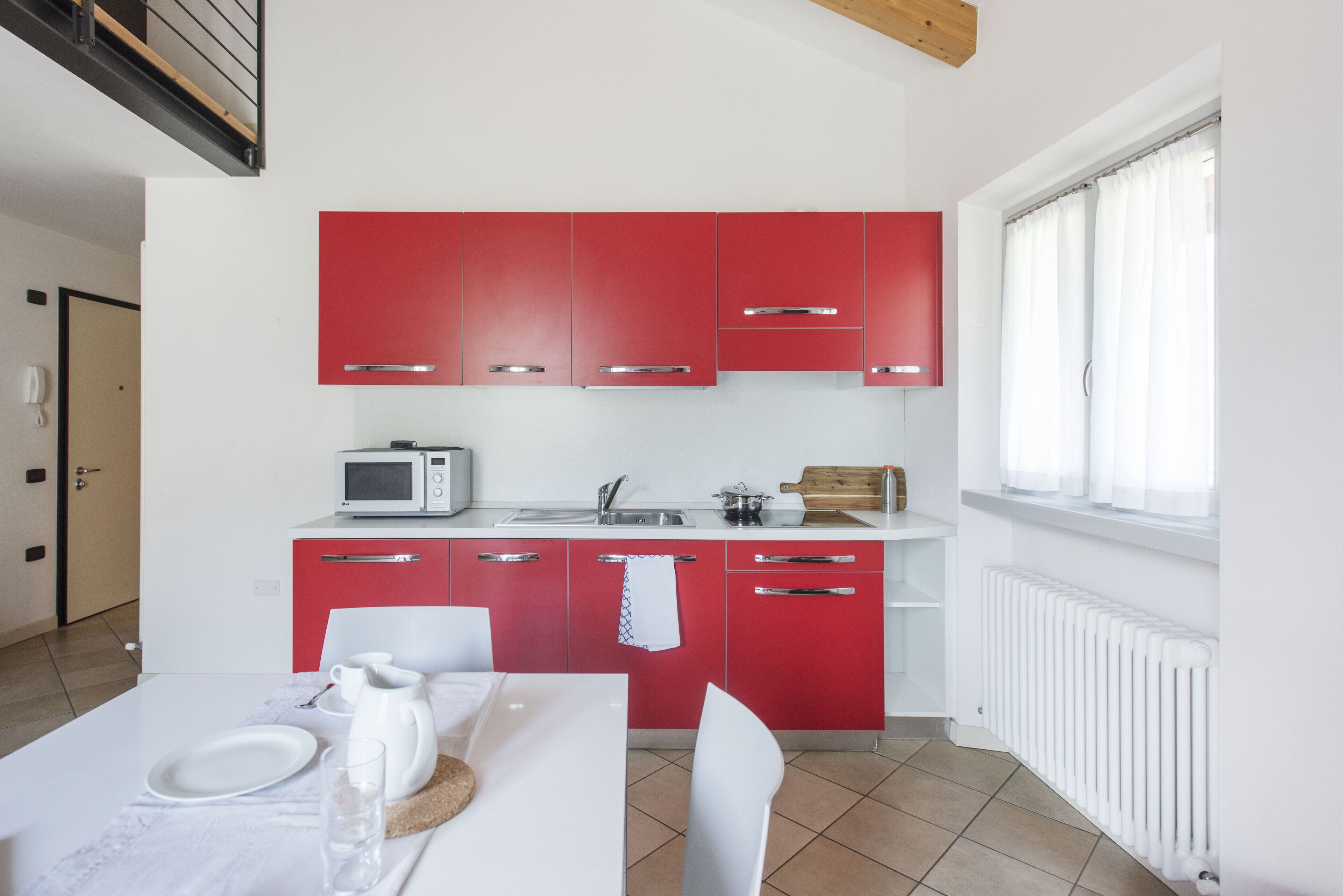 Una cocina moderna con armarios rojos, encimeras blancas, un microondas y una zona de comedor con una mesa dispuesta para dos.