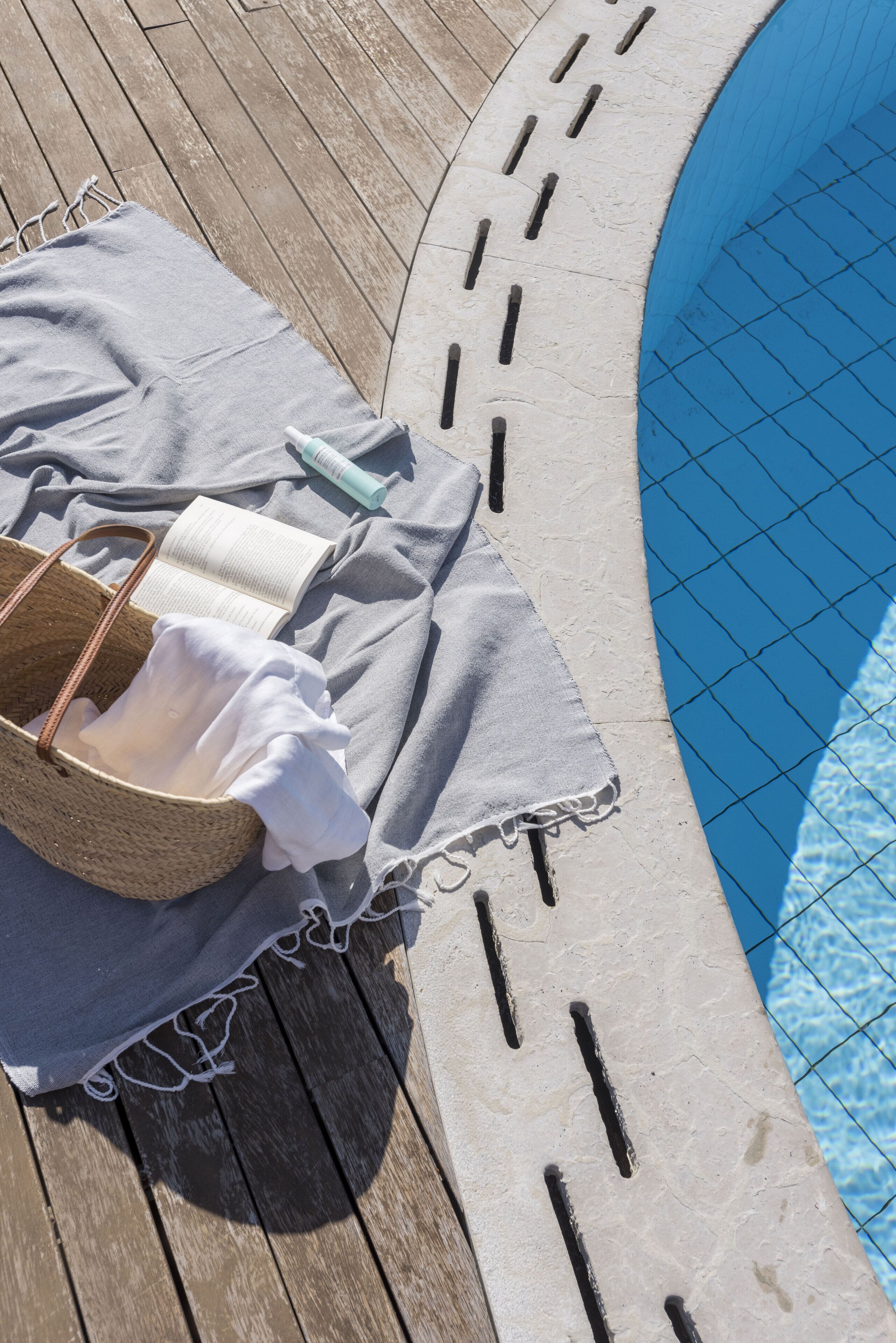 A poolside area with a wooden deck, a lounge chair, a towel, and a wicker basket.