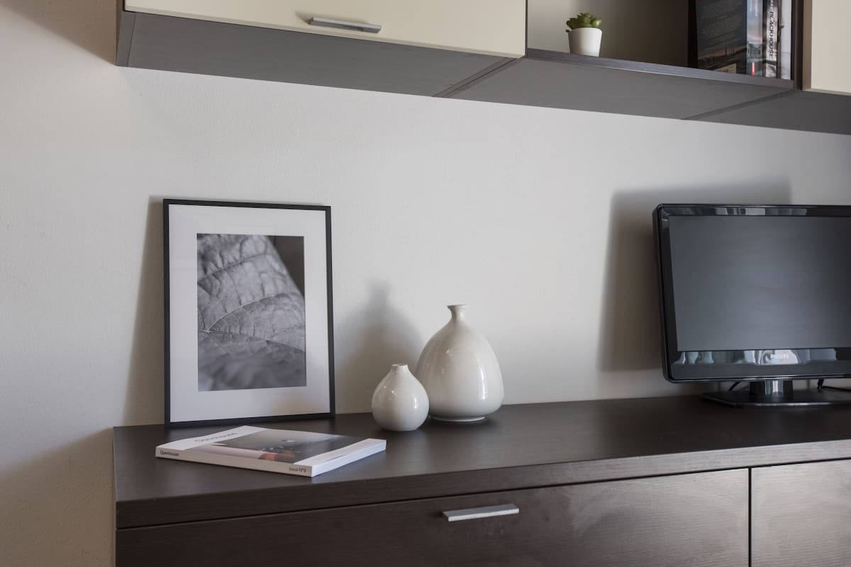 Un bureau en bois foncé orné d’une photographie encadrée, deux vases blancs, un livre et un écran Philips.