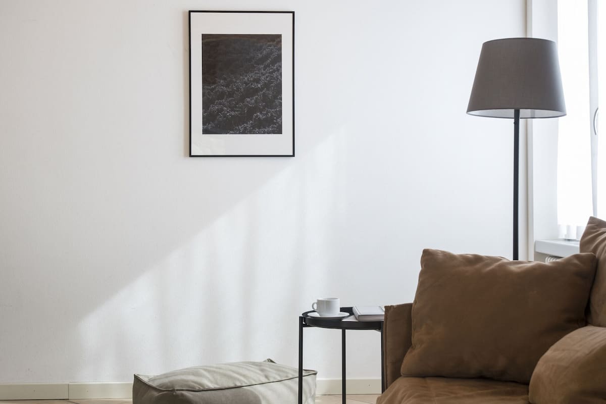 Une chambre moderne avec un plafond en bois, un lit avec une literie marron, une table de chevet avec une lampe, un tableau encadré au mur et un fauteuil poire sur le sol.