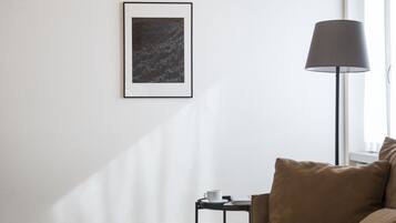 A modern room with a wooden ceiling, a bed with brown bedding, a side table with a lamp, a framed picture on the wall, and a bean bag on the floor.