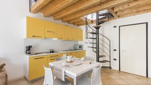 Een moderne keuken met gele kastjes, een witte tafel en een spiltrap.