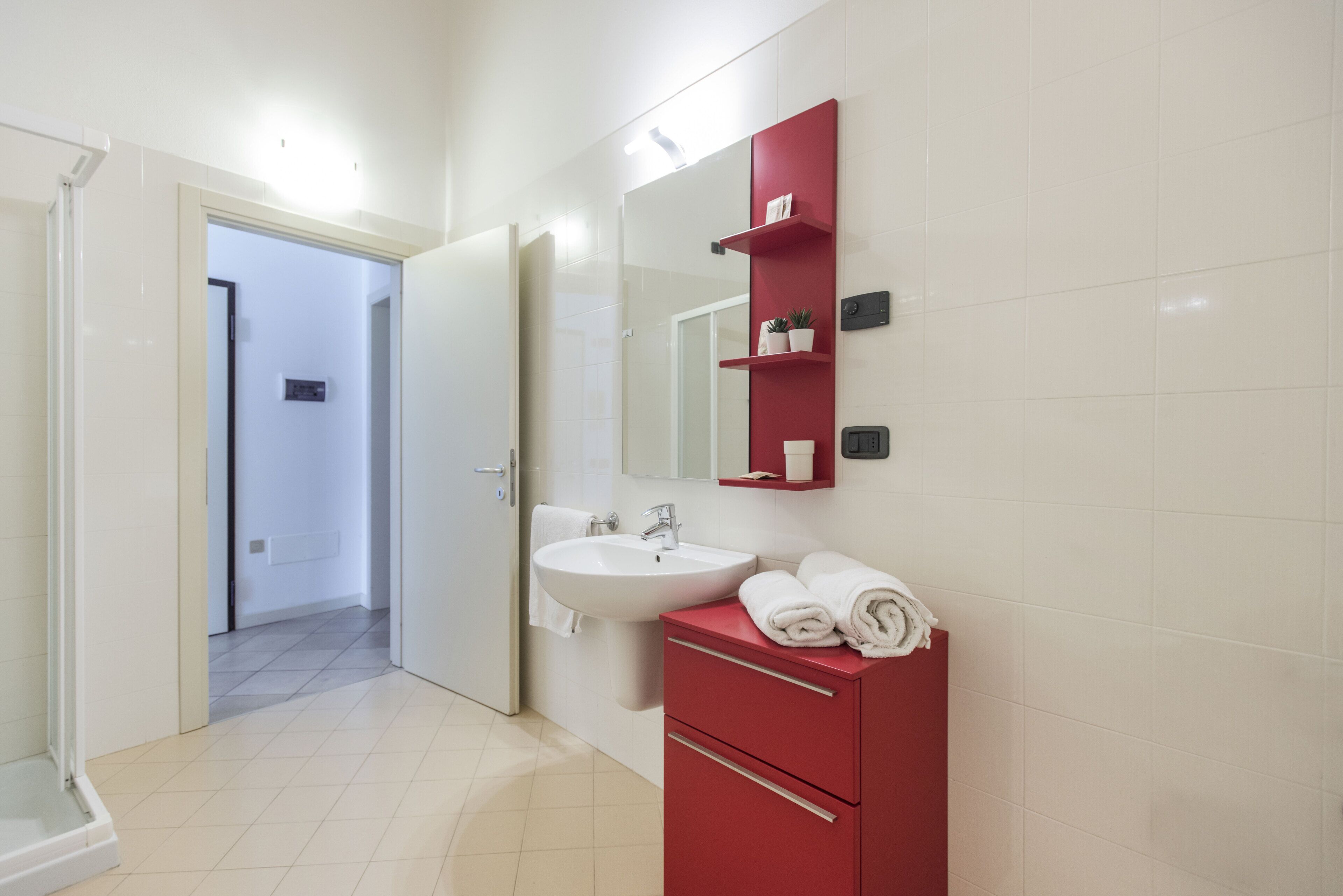 Un baño moderno con un lavamanos blanco, tocador rojo y un espejo grande.