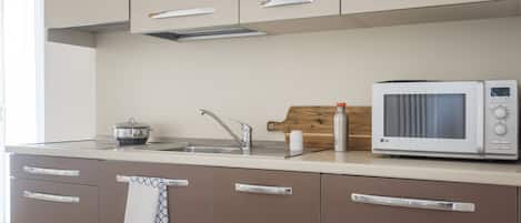 Una cocina moderna con microondas, pileta y tabla de cortar de madera.