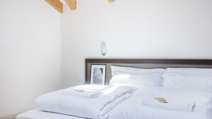 Een opgemaakt bed met witte lakens, een houten hoofdbord en een ingelijste foto aan de muur.