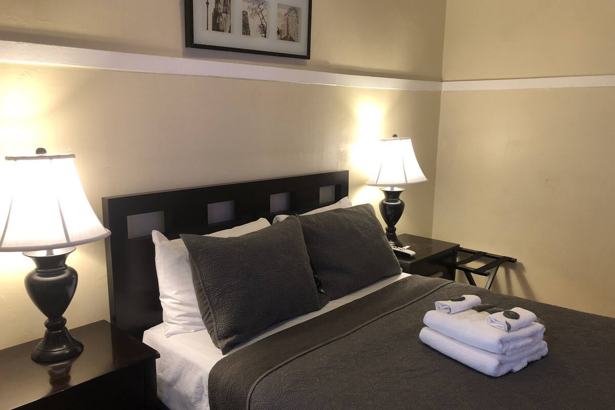 A neatly made bed with a dark headboard, two bedside tables with lamps, and a framed picture on the wall.