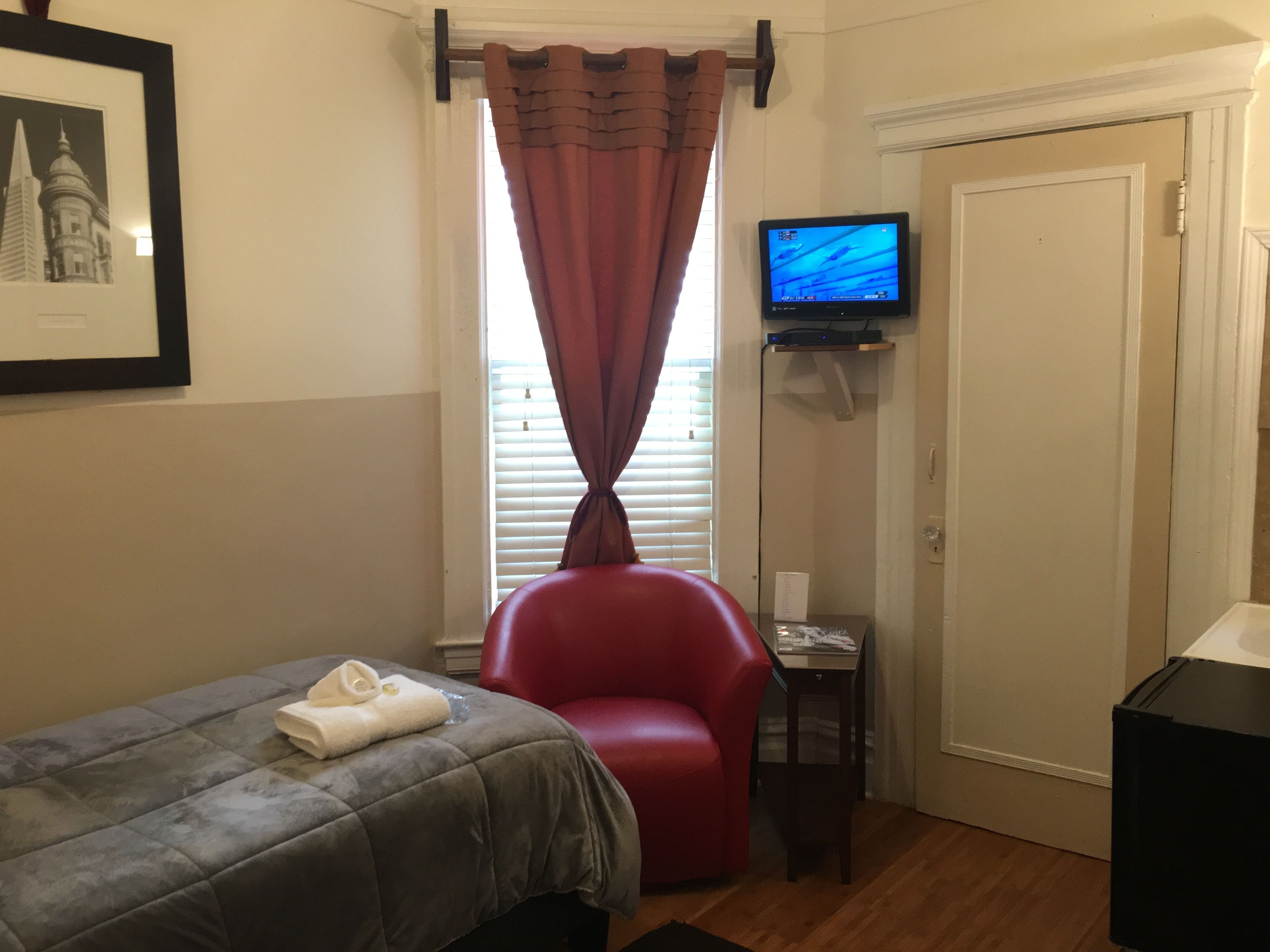 Une chambre d’hôtel avec un lit, un fauteuil rouge, un téléviseur posé sur un meuble et une porte.