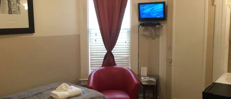 Une chambre d’hôtel avec un lit, un fauteuil rouge, un téléviseur posé sur un meuble et une porte.