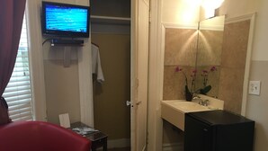 A hotel room with a TV mounted on the wall, a red chair, a small table with a magazine, and a bathroom with a sink and mirror. - Luz Hotel (San Francisco)