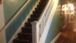 A staircase with dark carpeted steps and white balusters, leading to a landing with a patterned carpet. - Luz Hotel (San Francisco)