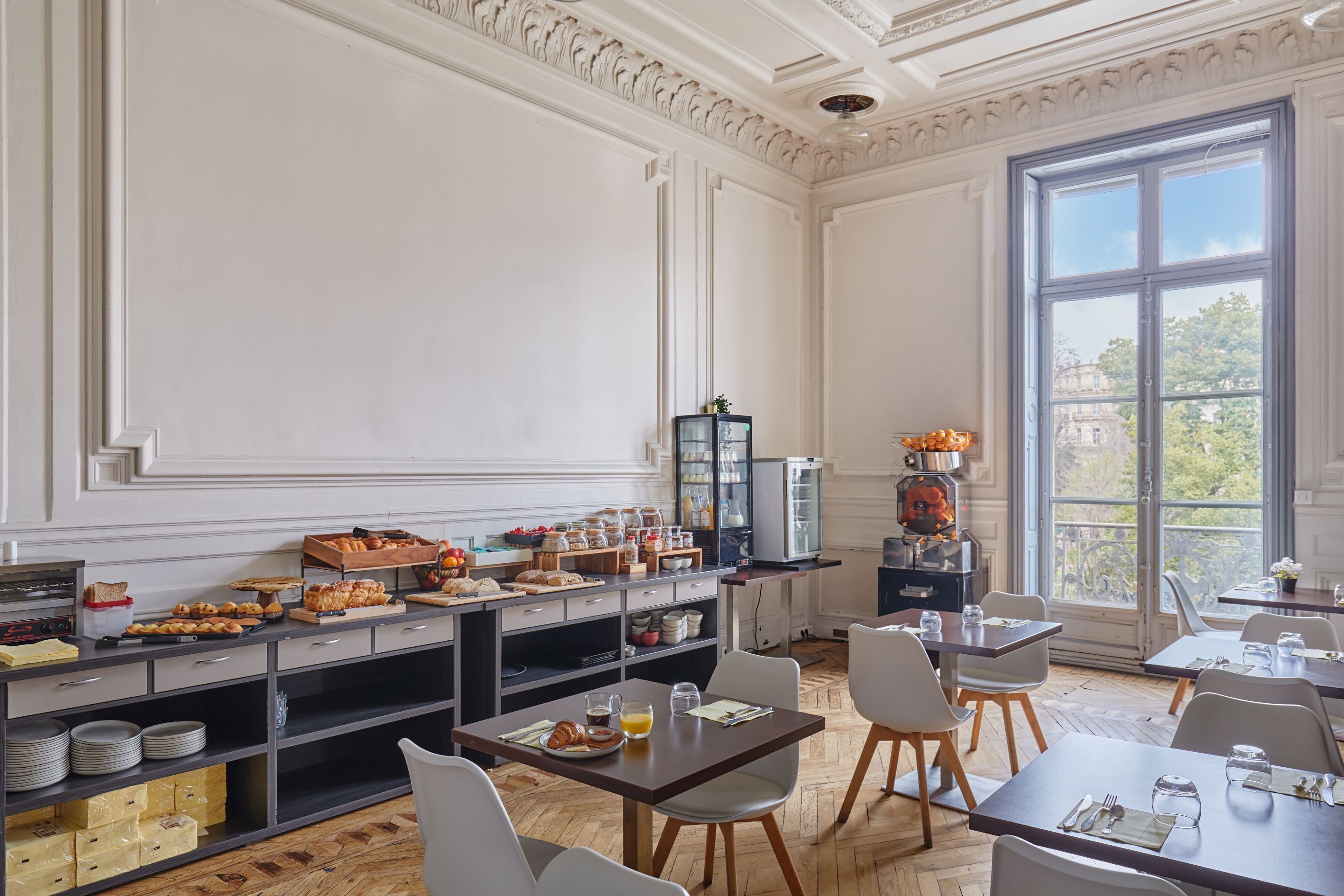 Un bufé de desayuno con diversas opciones de comida y un amplio ventanal con vistas a edificios y árboles.