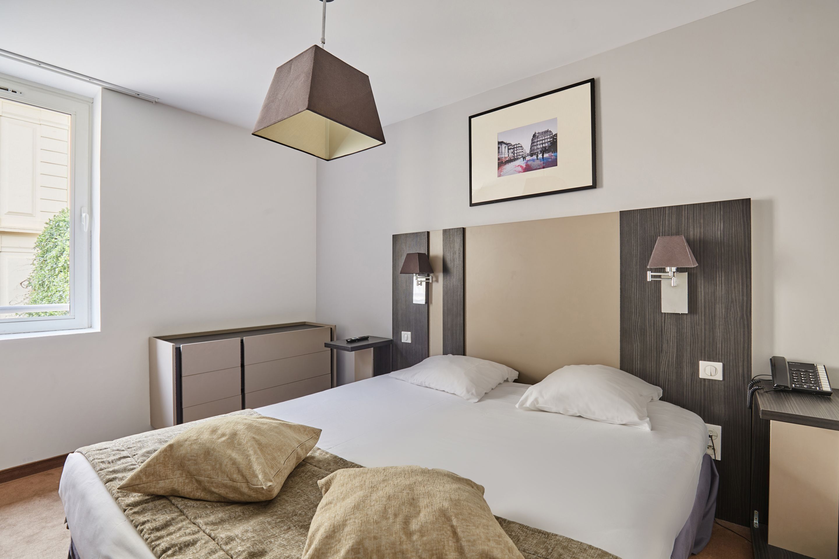 Ein modernes Hotelzimmer mit einem großen Bett, Nachttischlampen, einem Schreibtisch mit Telefon und einem gerahmten Bild an der Wand.