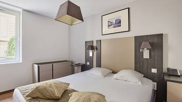 Ein modernes Hotelzimmer mit einem großen Bett, Nachttischlampen, einem Schreibtisch mit Telefon und einem gerahmten Bild an der Wand.