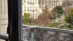 Une vue depuis un balcon orné de balustrades en métal ouvragé, donnant sur un parc et des bâtiments historiques à étages, dotés de balcons.