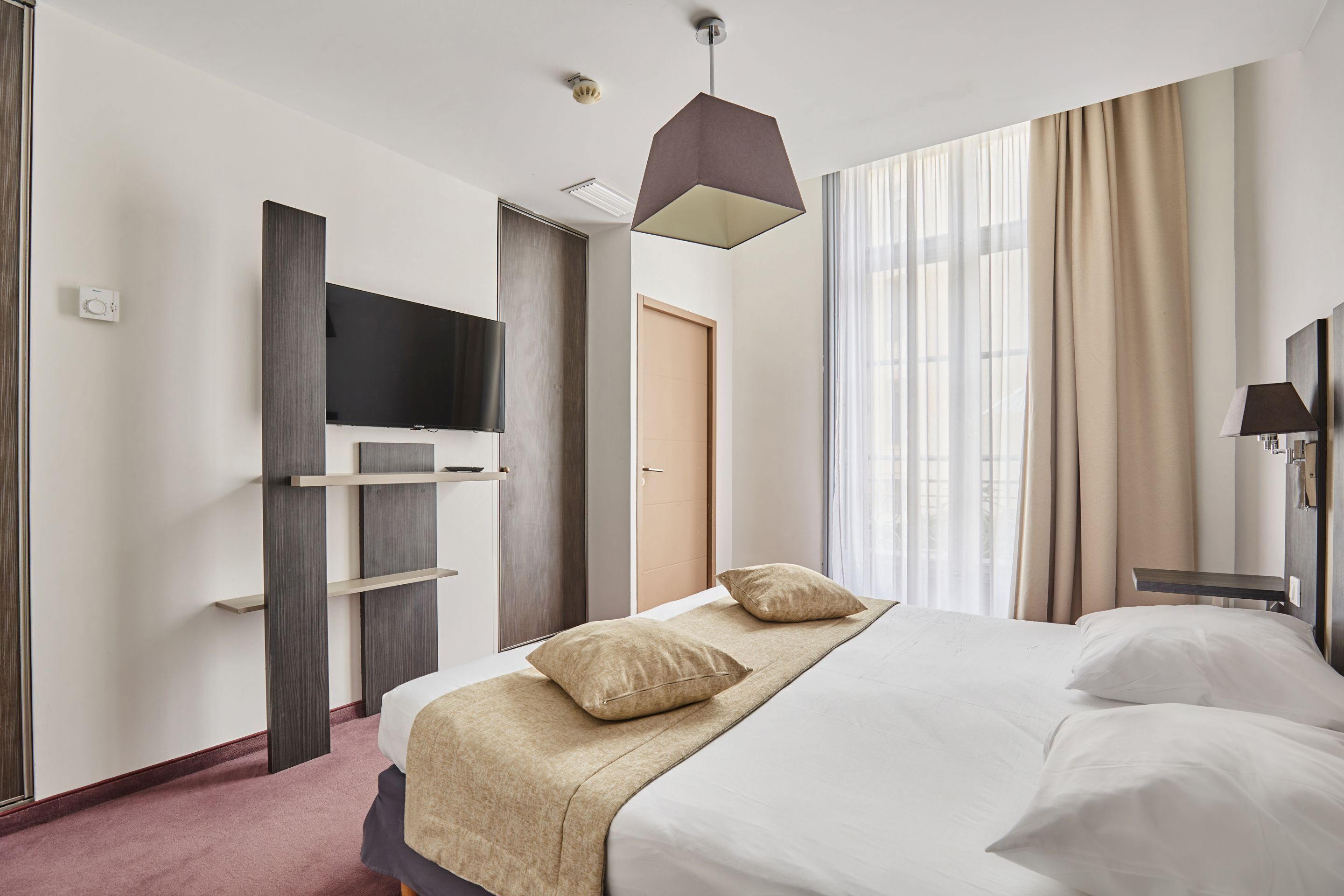 Habitación de hotel con cama, televisor de pantalla plana, escritorio y ventana con cortinas.