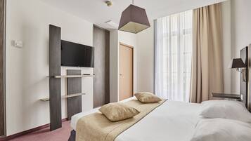 Habitación de hotel con cama, televisor de pantalla plana, escritorio y ventana con cortinas.