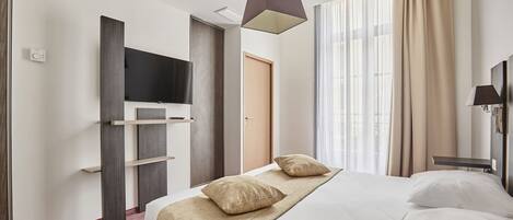Habitación de hotel con cama, televisor de pantalla plana, escritorio y ventana con cortinas.