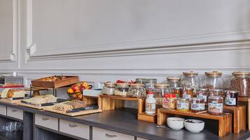 A breakfast buffet with various breads, fruits, and jars of spreads.