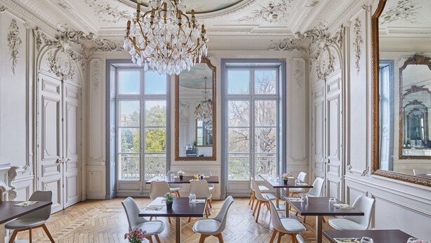 Un espace repas agrémenté de détails décoratifs au plafond, de grandes fenêtres et d’un lustre.